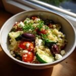 A close-up of a Delightful Mediterranean Bowl filled with quinoa, cherry tomatoes, cucumber, olives, and feta cheese.