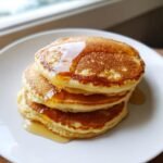 A stack of three fluffy pancakes drizzled with syrup, made with our easy basic pancakes recipe.