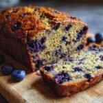 A slice of Irresistibly Fluffy Blueberry Zucchini Bread on a wooden board with fresh blueberries.