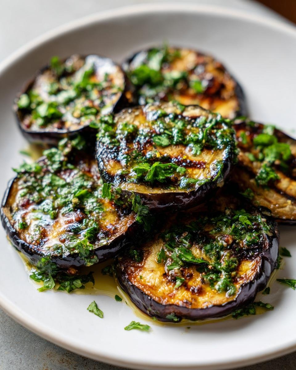 Close-up of perfectly Grilled Eggplant With Garlic Vinaigrette slices drizzled with oil and topped with fresh parsley.