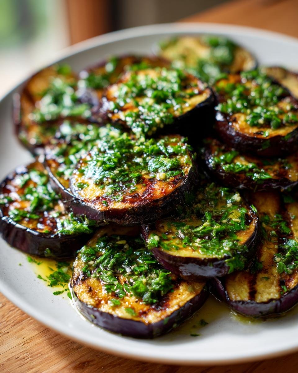 Close-up of grilled eggplant slices topped generously with bright green garlic vinaigrette.