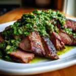 Close-up of sliced Grilled Flank Steak With Avocado Chimichurri, showing medium-rare interior and bright green sauce.