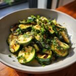 Close-up of a bowl filled with slices of Grilled Zucchini Salad, tossed with herbs and dressing.