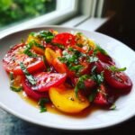 Close-up of a bright Heirloom Tomato Salad featuring sliced red and yellow tomatoes drizzled with dressing and fresh basil.