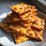 A tempting stack of golden brown, flaky Homemade Cheese Crackers sprinkled with coarse sea salt.