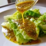 A close-up of Homemade Italian Salad Dressing being poured from a spoon onto crisp green lettuce leaves.