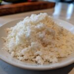 Close-up of a mound of freshly made cauliflower rice in a white bowl, ready for cooking or storage.