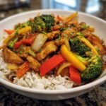 A bowl of Irresistible Asian Stir Fry with chicken, broccoli, bell peppers, and onions served over white rice.