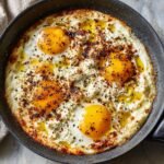 Close-up of Irresistible Baked Feta Eggs in a skillet, with runny yolks and sprinkled spices.