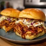 Two Irresistible BBQ Chicken Sliders piled high with pulled chicken and coleslaw on a blue plate.