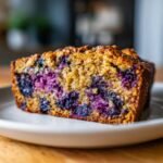 A close-up shot of a slice of Irresistible Blueberry Zucchini Bread, showcasing plump blueberries and a golden-brown crumb.