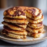 A tall stack of Irresistible Cinnamon Brown Sugar Pancakes, golden brown with visible cinnamon sugar topping.