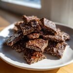 A pile of Irresistible Healthy Dark Chocolate Quinoa Crisps on a light gray plate, showing the texture of quinoa seeds embedded in dark chocolate.