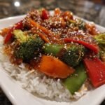 Close-up of Irresistible Vegetable Stir Fry with broccoli, peppers, carrots, and snow peas over white rice, topped with sesame seeds.