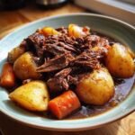 A close-up of a bowl filled with tender pot roast, chunks of potatoes, and carrots in a rich gravy.