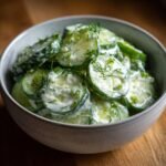 A close-up of a bowl filled with refreshing creamy cucumber salad, garnished with fresh dill.