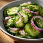Close-up of a Refreshing Cucumber Vinegar Salad with thinly sliced cucumbers, red onion rings, and dill in a white bowl.