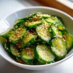 Close-up of a refreshing easy Asian cucumber salad in a white bowl, topped with sesame seeds.