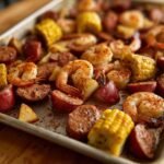 Close-up of a Sheet Pan Shrimp Boil featuring seasoned shrimp, smoked sausage slices, red potatoes, and corn on the cob.