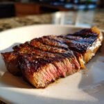 Close-up of a perfectly cooked thin steak, sliced and served on a white plate, showcasing its pink interior.