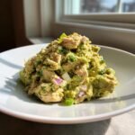 A mound of creamy Tuna Salad Avocado mixture with visible chunks of tuna, red onion, and green onion on a white plate.