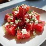 Close-up of vibrant Watermelon Salad cubes topped with crumbled feta cheese and fresh mint leaves.