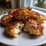 Close-up of several crispy, golden brown Air Fryer Crab Cakes on a white plate, one is broken open showing the flaky interior.