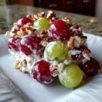 A close-up serving of creamy Grape Salad featuring red and green grapes coated in dressing and topped with chopped pecans.