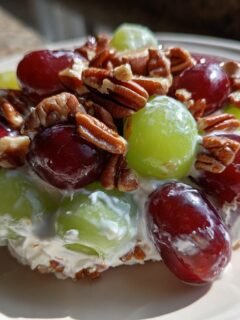 A close-up serving of creamy Grape Salad topped with red and green grapes and crunchy pecans.