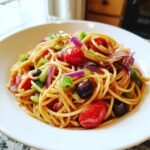 A close-up serving of vibrant Spaghetti Salad featuring cherry tomatoes, green peppers, red onion, and black olives.