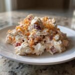 A mound of creamy Apples Cheddar Chicken Salad featuring shredded chicken, red apple chunks, and shredded cheddar cheese on a white plate.