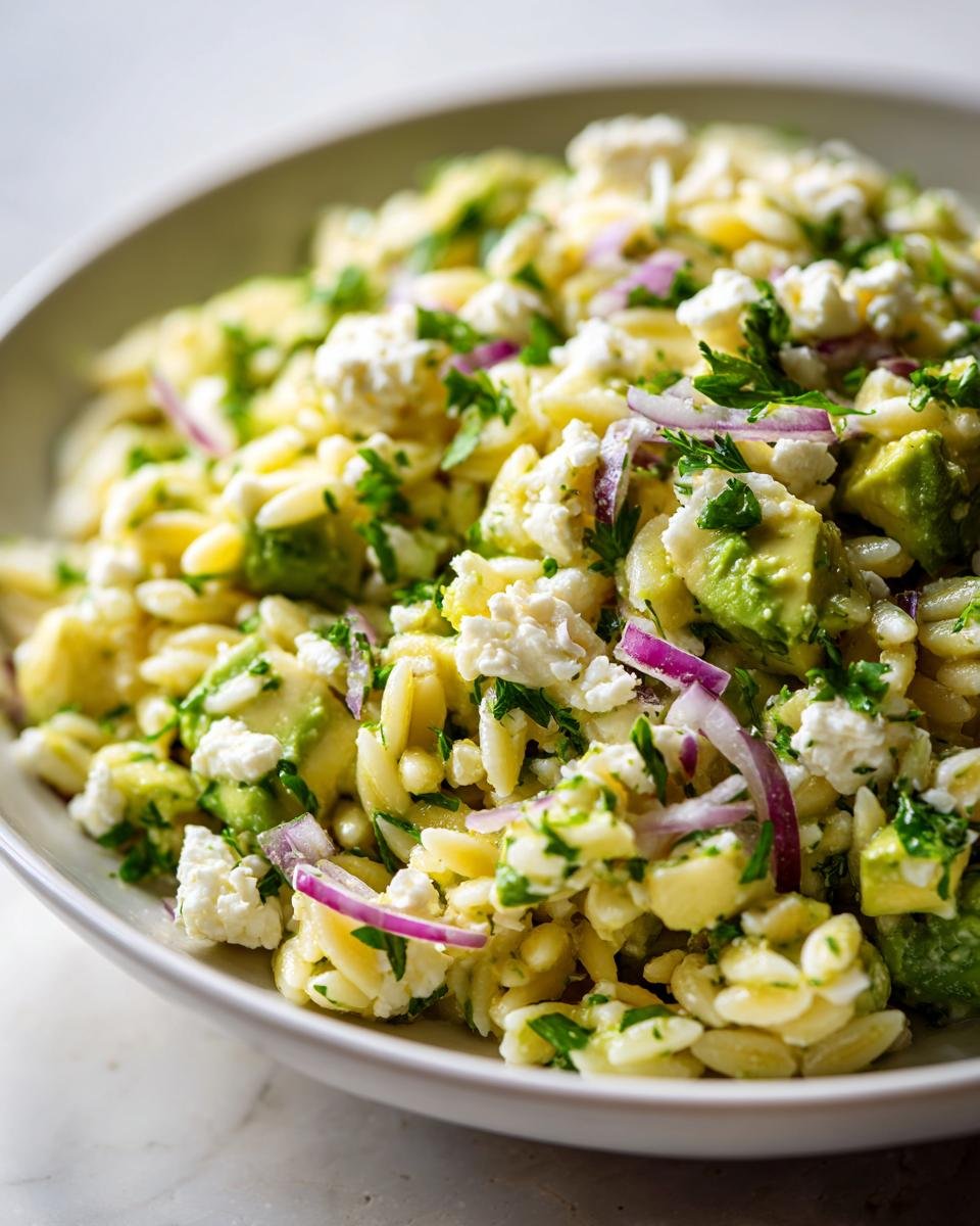 Close-up of a vibrant Avocado Feta Orzo Salad featuring orzo pasta, chunks of avocado, feta cheese, and red onion.