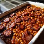 Close-up of rich, saucy Baked Beans With Smoked Sausage slices baked in a white casserole dish.