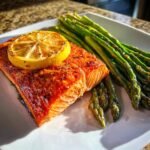 A perfectly cooked fillet of Baked Sockeye Salmon With Asparagus, topped with a lemon slice.