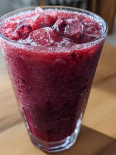 Close-up of a tall glass filled with vibrant, deep red Berry Wine Slushies topped with crushed ice.