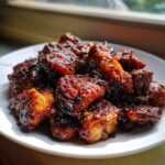 Close-up of glistening, dark glazed Black Pepper Chicken pieces piled on a white plate, ready to serve.