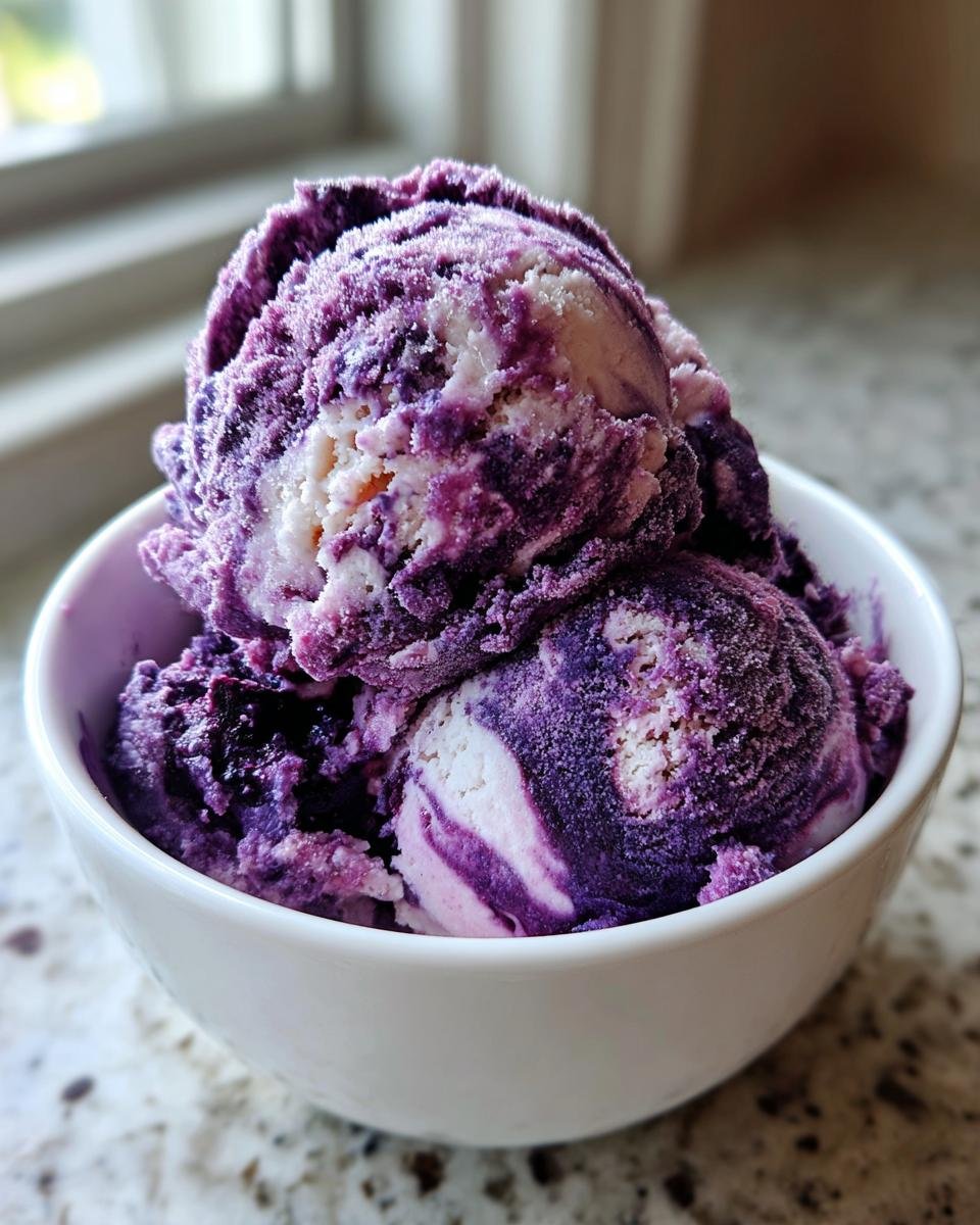 Three scoops of vibrant purple and white swirled Blueberry Nice Cream served in a white bowl.