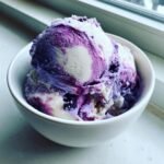 Two scoops of swirled purple and white Blueberry Nice Cream served in a small white bowl near a window.
