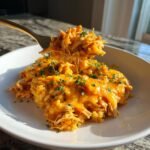 A fork lifts a cheesy, saucy scoop of Buffalo Chicken Rice Casserole topped with fresh parsley.