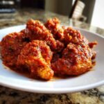 Close-up of tender chicken pieces generously coated in a vibrant red Chicken Tomato Sauce, sprinkled with herbs.