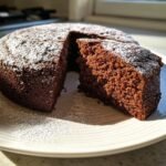 A rich, dark Chocolate Olive Oil Cake dusted with powdered sugar, with one slice cut out showing the moist crumb.