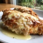 Close-up of a golden, breaded chicken fillet topped with melted cheese, served in a pool of creamy sauce: Creamy Chicken Francaise.