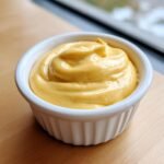 Close-up of thick, creamy, bright yellow Honey Mustard Sauce swirled in a small white ramekin.