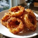 A close-up of several golden brown, perfectly breaded Crispy Air Fryer Onion Rings stacked on a white plate.