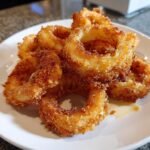 Close-up of a pile of perfectly golden and crispy Onion Rings served on a white plate.