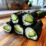 A stack of five freshly made Cucumber Sushi Rolls featuring cucumber, cream cheese, and rice wrapped in nori.