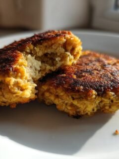 Two golden brown, pan-fried Easy Chickpea Patties on a white plate, one broken in half showing the soft interior.