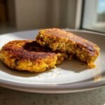 Two golden brown Easy Chickpea Patties on a white plate, one cut in half showing the textured interior.