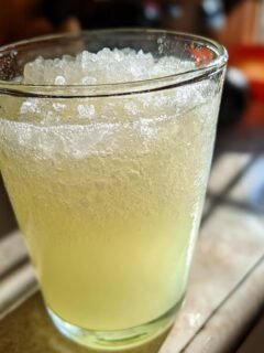 Close-up of a tall glass filled with icy, pale yellow Frosted Lemonade, topped with crushed ice.