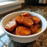 A white bowl filled with thick, glazed slices of Candied Yams glistening in a sweet syrup.